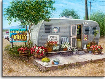 A small well-worn travel trailer sits alongside Route 66 in Needles, California, next to a sign offering Mystic Maze Honey for sale. Baskets, barrels and pots hold brightly colored flowers in front of the trailer and its open door. A thermometer hanging on the trailer shows a hot, 100 degree day, while a large sign advertises Pure Local Honey.